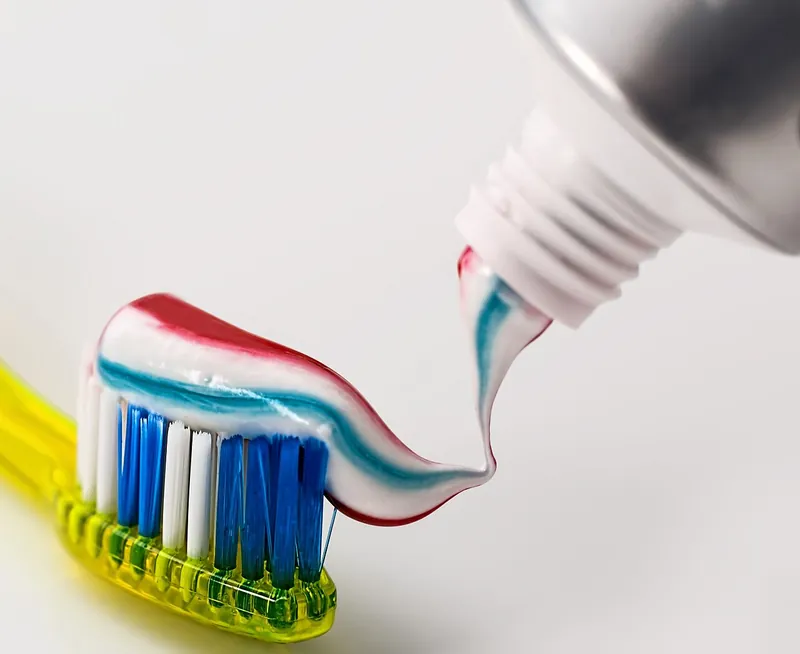 Striped red, white and blue human toothpaste being squeezed from a tube onto a yellow toothbrush with blue and white bristles