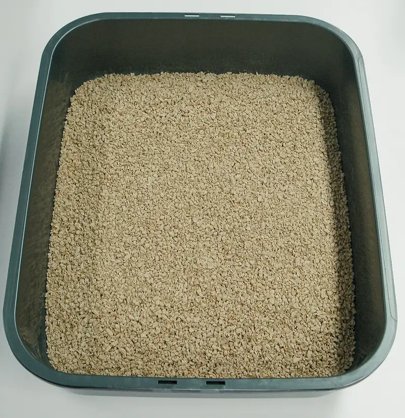 A dark grey litter tray seen from above, filled evenly with light beige granular plant based clumping litter