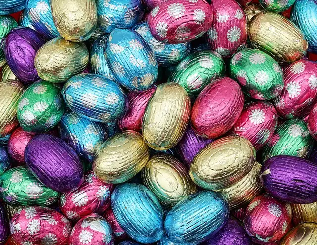 A pile of small chocolate Easter eggs wrapped in shiny pink, blue, green, gold and purple foil with a flower pattern