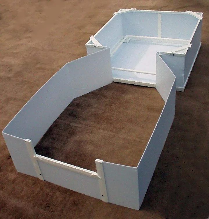 White plastic whelping box with low walls and inside rails, connected to a larger open extension pen on a dirt floor